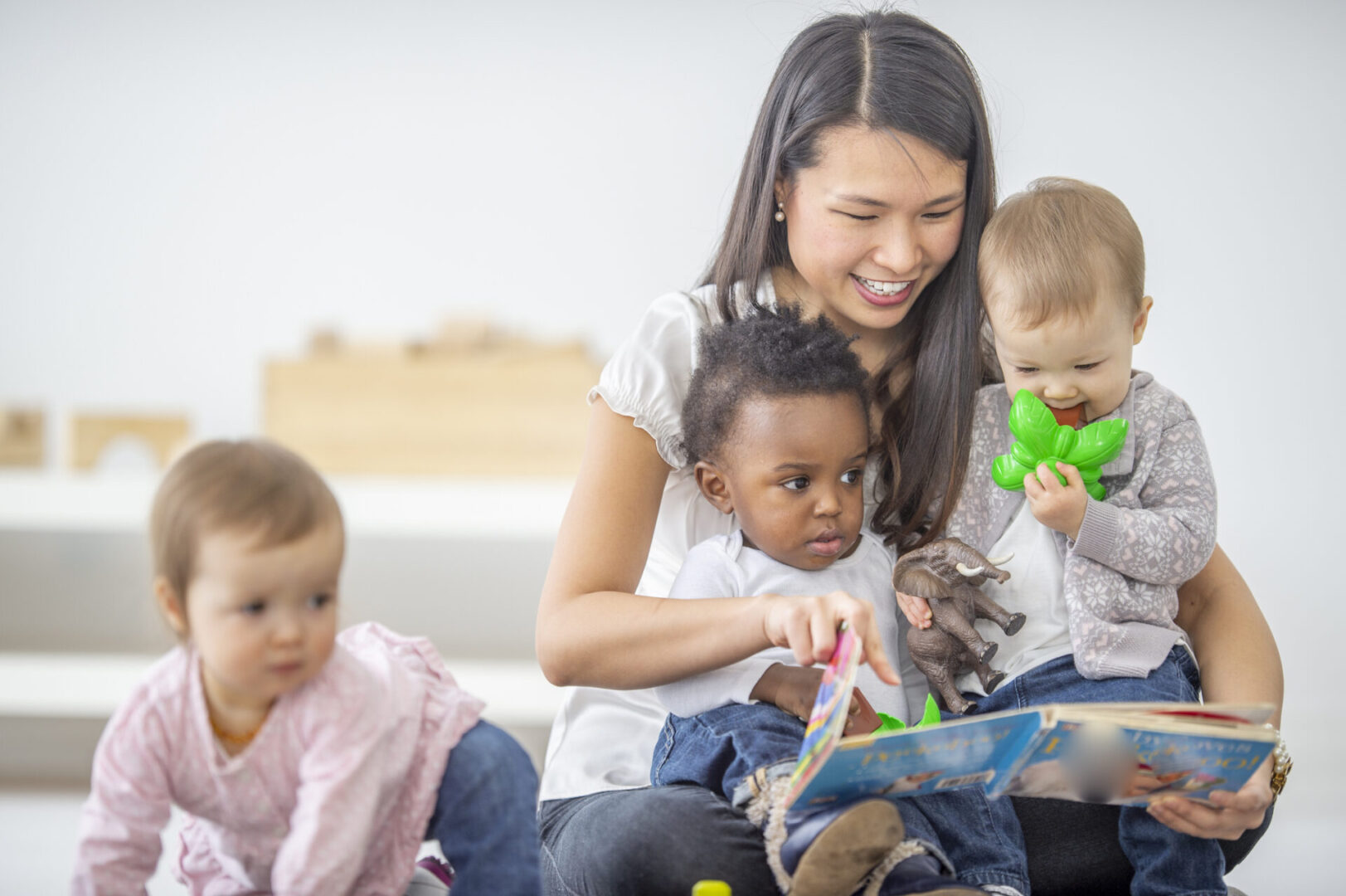 A female Asian preschool teacher is reading a book to her group of children.