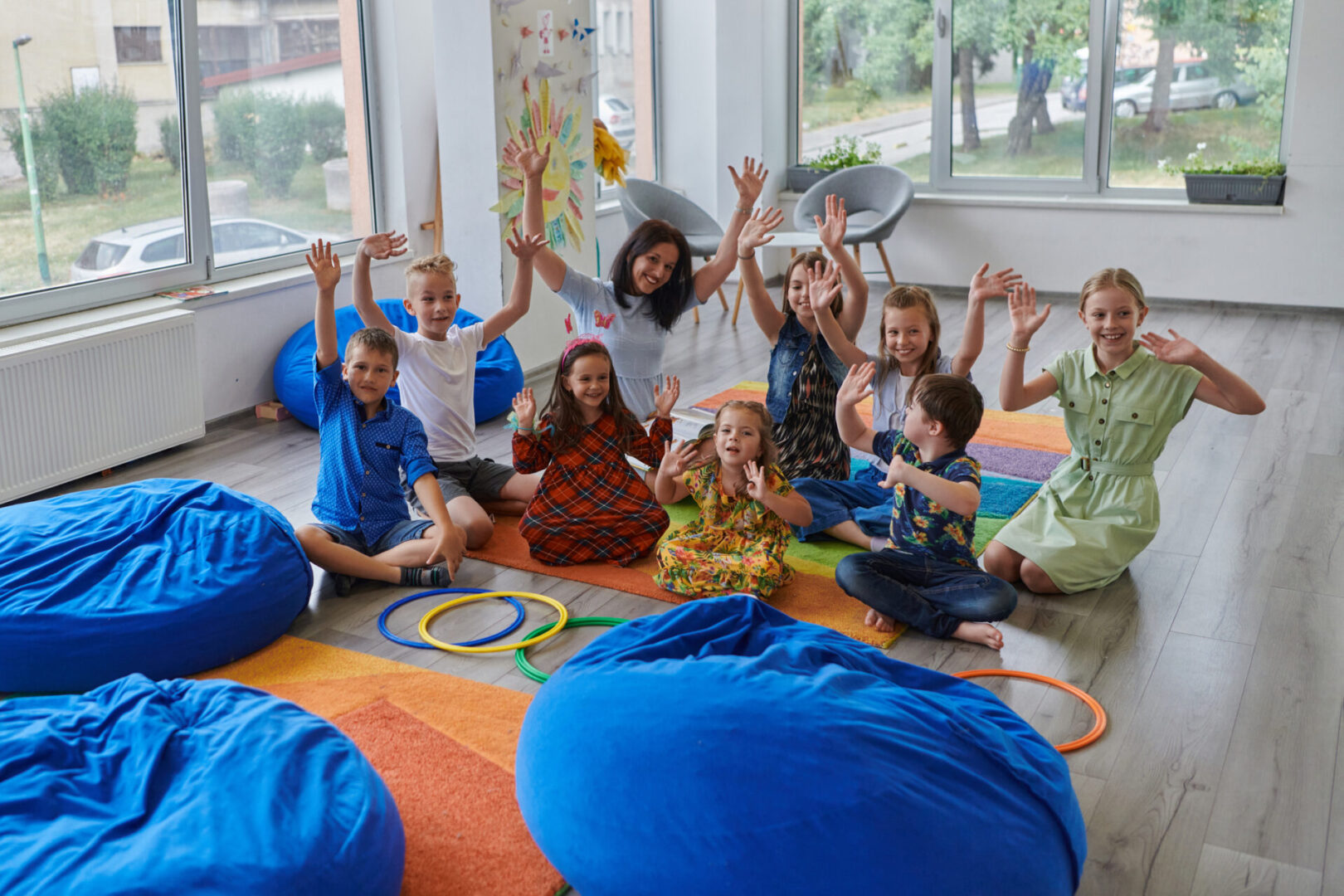 A happy female teacher sitting and playing hand games with a group of little schoolchildren.